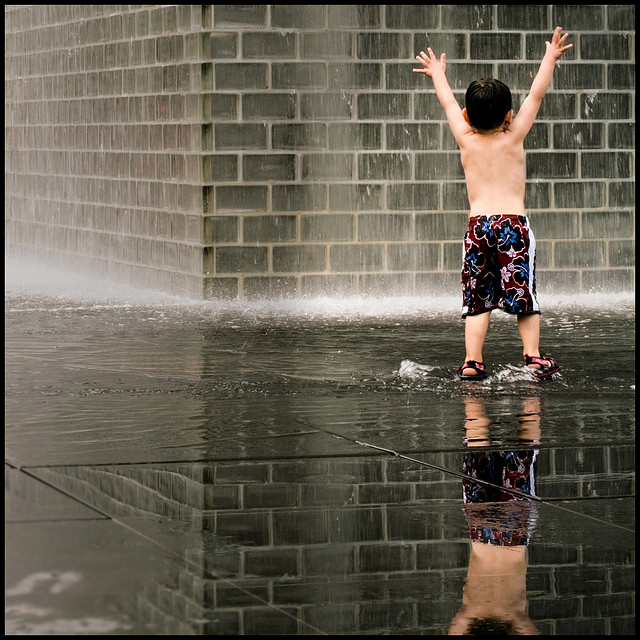 A picture of a boy playing in water in an urban setting. 